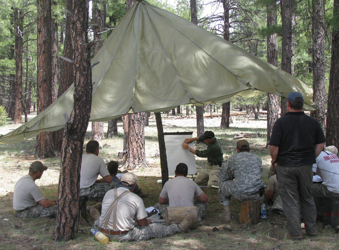 An Army group sitting under a parachute studying outdoor survival techniques.